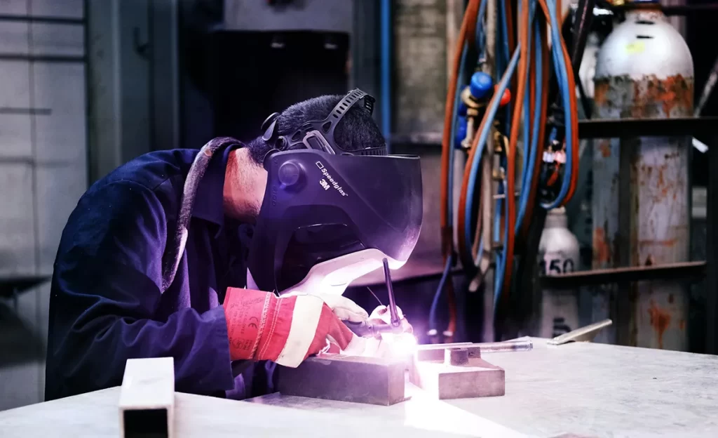 Welder wearing a protective mask while joining small metal components, illustrating the precision and demand of Welder / Fabrication jobs Scotland.