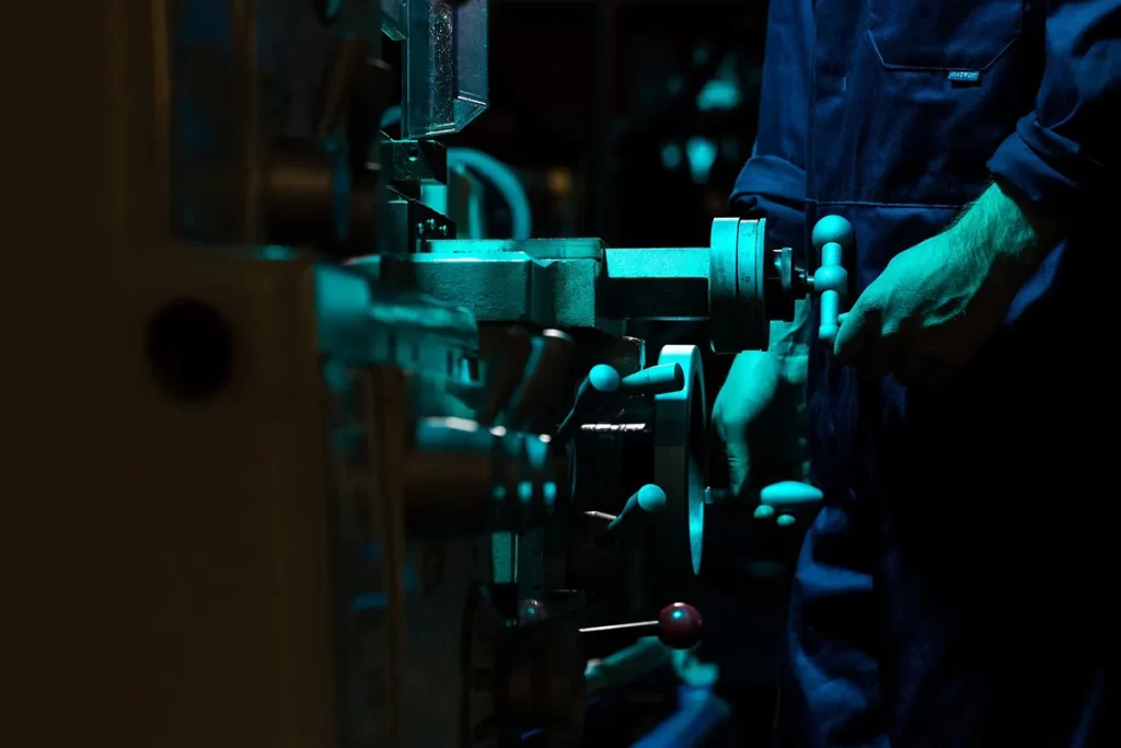 Close-up of a worker operating industrial machinery in a dimly lit workshop, representing Mechanical Fitter Jobs East Kilbride.